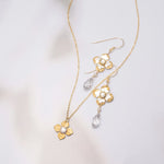 Octavia Gold Silver Earrings by Holly Yashi, inspired by Victorian style, feature clear teardrop crystals and are shown with a gold flower pendant necklace on a soft, light background.