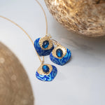 The Arabella Sapphire Blue Earrings by Holly Yashi feature bright blue, patterned pendants and dark blue gemstones, complemented by delicate glass beads and displayed near textured gold accents.