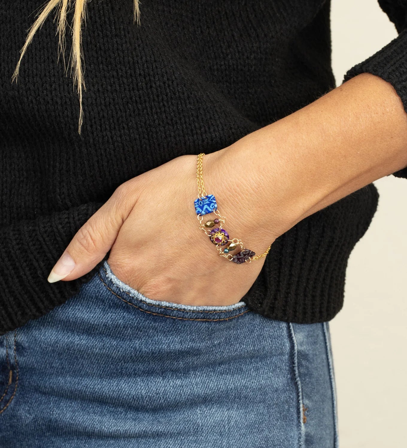 A person in a black sweater and blue jeans rests their hand in a pocket, showcasing the Holly Yashi Alex Multi Color Bracelet with vibrant, gem-inspired stones on their wrist.