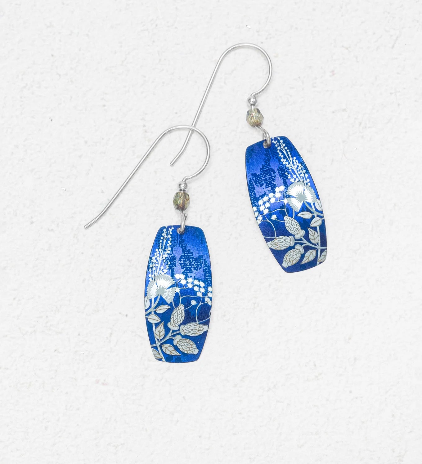 Falling Bloom Indigo Earrings by Holly Yashi: blue, oval-shaped handcrafted earrings with silver floral patterns and hooks, displayed on a light textured background.