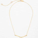 The Zara Bar Gold Necklace by Holly Yashi features a thin gold chain and curved bar pendant for a minimalist look. Hypoallergenic and stylish, this piece from Holly Yashi is shown on a white textured background.