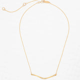 The Zara Bar Gold Necklace by Holly Yashi features a thin gold chain and curved bar pendant for a minimalist look. Hypoallergenic and stylish, this piece from Holly Yashi is shown on a white textured background.