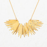 The Aster Necklace-Gold Necklace by Holly Yashi features a sunburst design with jagged rays and sparkling crystals, radiating golden brilliance against a plain white background.