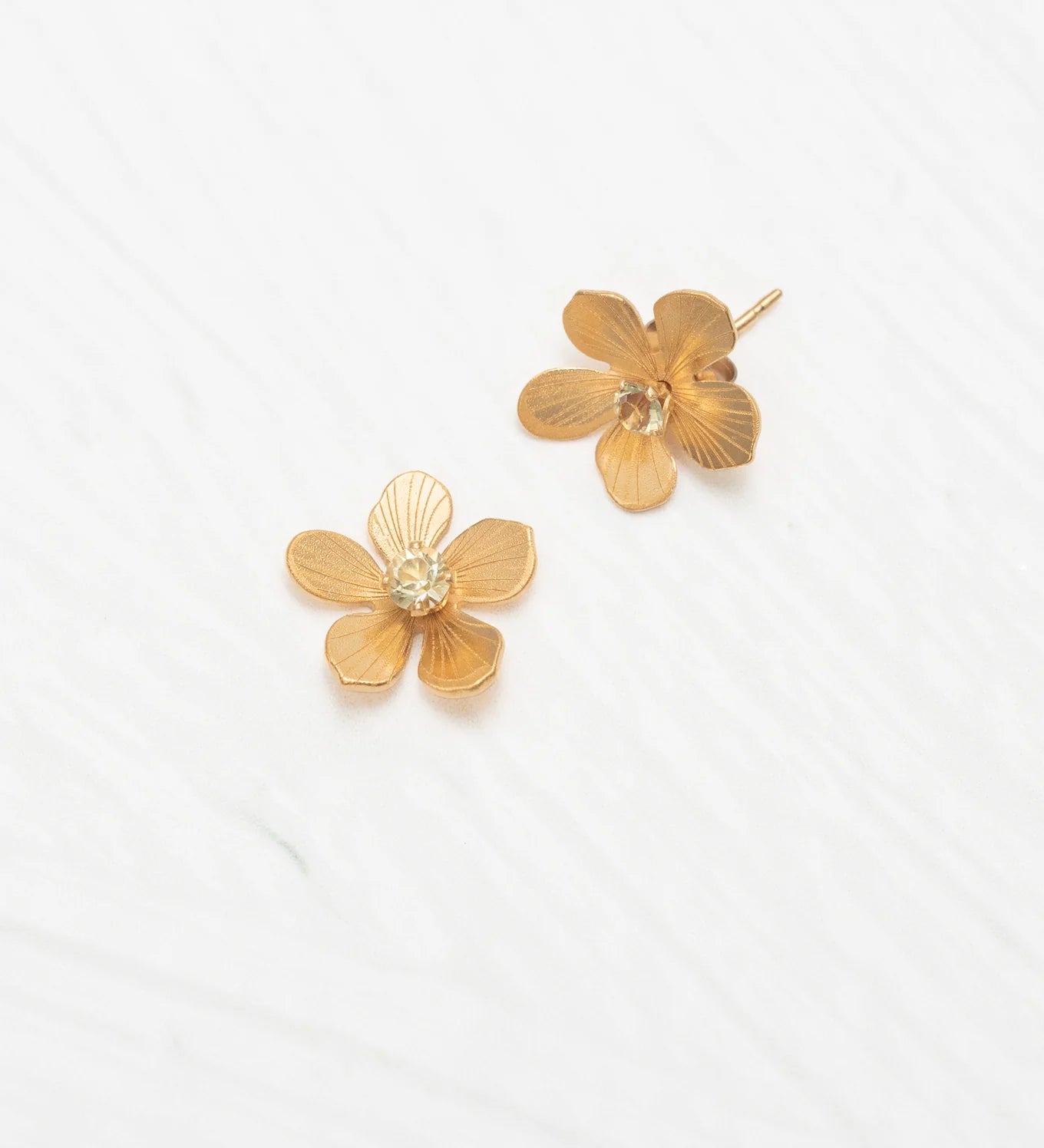 The Petite Plumeria Post Gold/Champagne Earrings by Holly Yashi feature textured flower-shaped studs with sparkling champagne centers, set on gold-filled posts—a charming accessory for any garden party, shown against a white textured background.