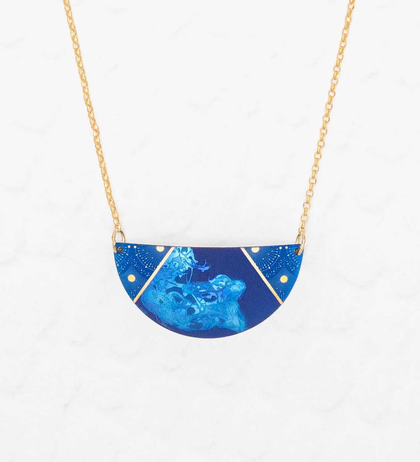 The Holly Yashi Orion Pendant/ Midnight Blue Necklace features a half-circle pendant with subtle floral designs and gold accents on a gold chain, displayed against a white textured background.