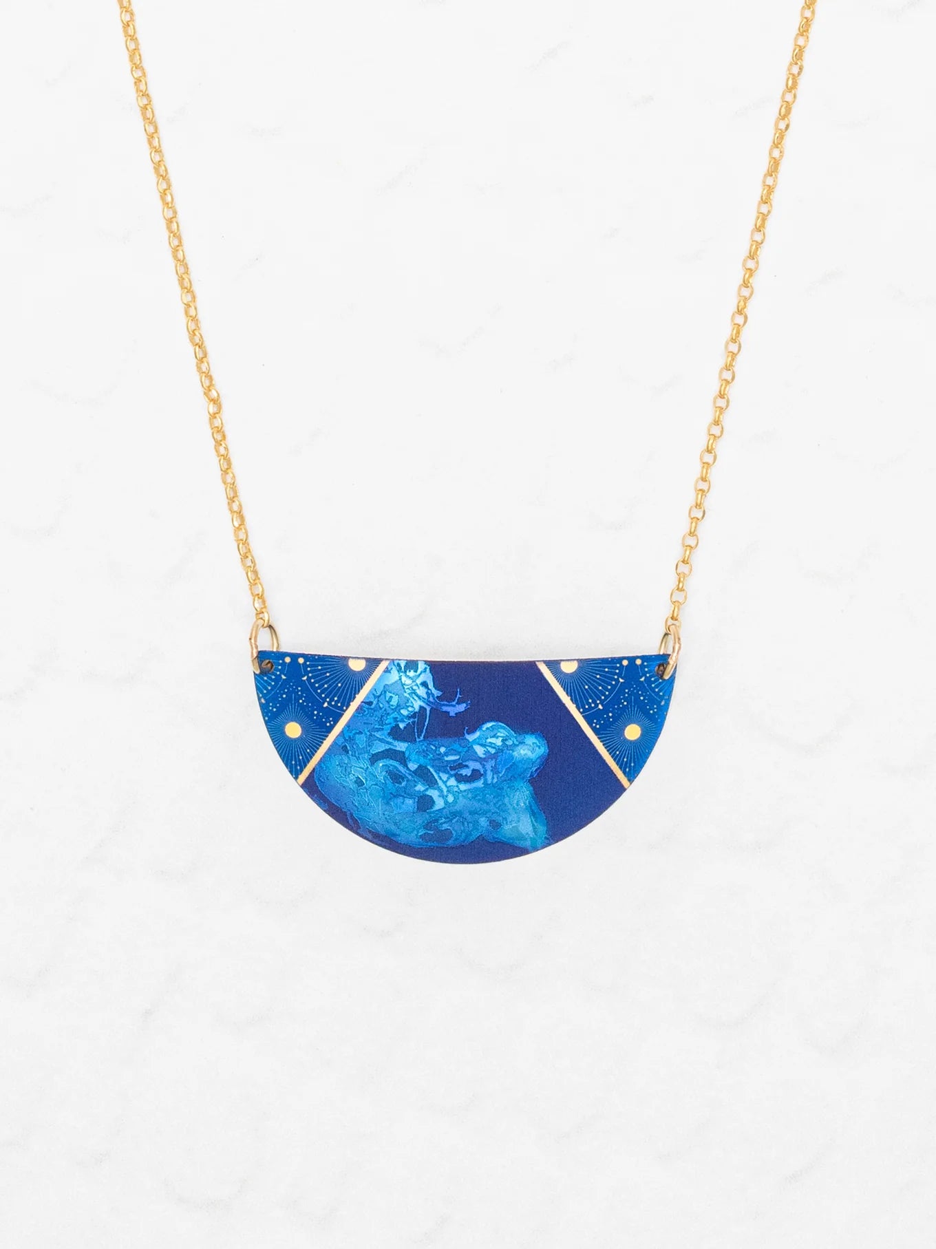 The Holly Yashi Orion Pendant/ Midnight Blue Necklace features a half-circle pendant with subtle floral designs and gold accents on a gold chain, displayed against a white textured background.