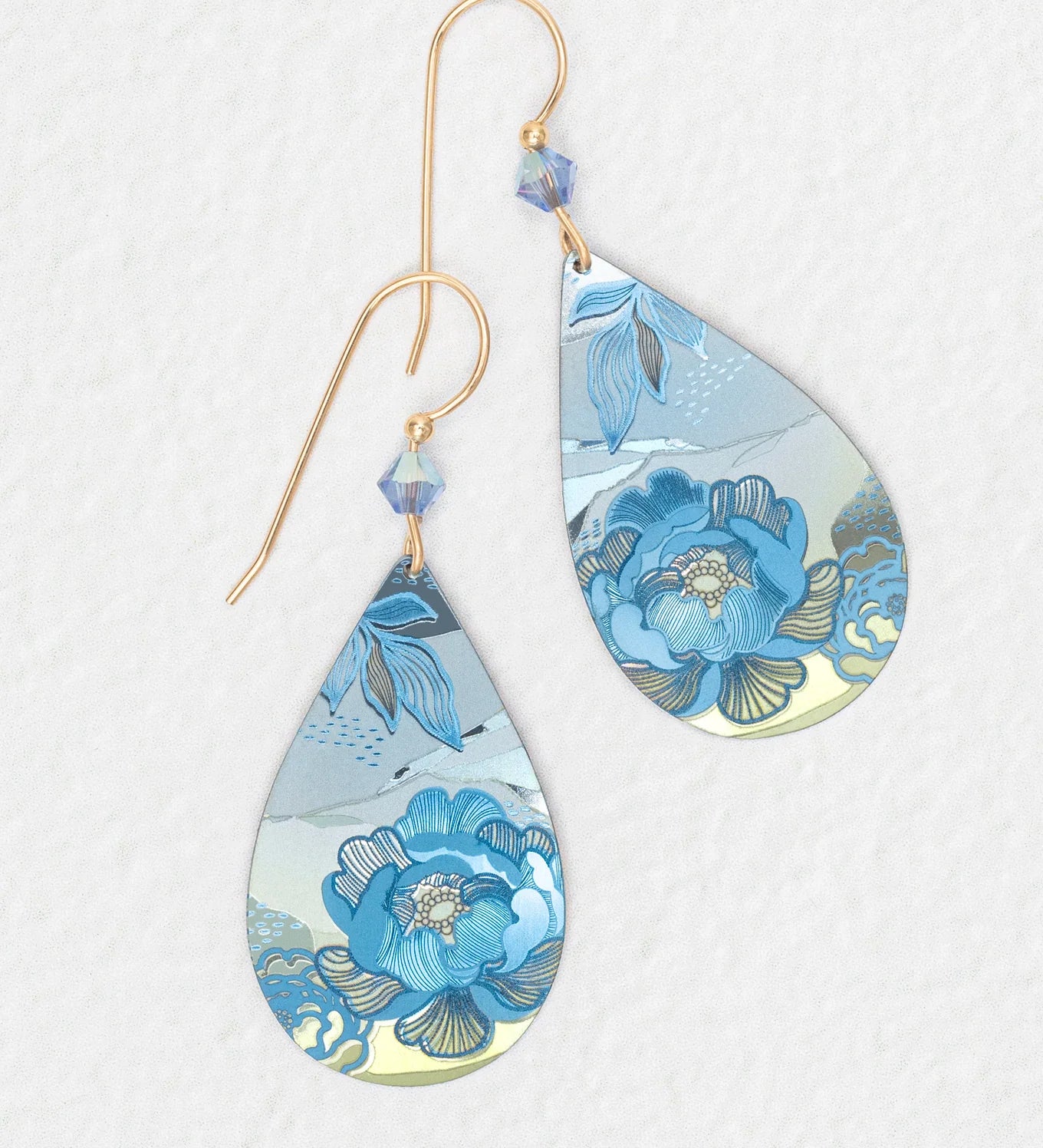 The Cynthia Sky Blue Earrings by Holly Yashi feature gold hooks, blue bead accents, and a sky blue floral pattern with silver on a white textured background. Hypoallergenic and ideal for sensitive ears.