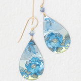 The Cynthia Sky Blue Earrings by Holly Yashi feature gold hooks, blue bead accents, and a sky blue floral pattern with silver on a white textured background. Hypoallergenic and ideal for sensitive ears.