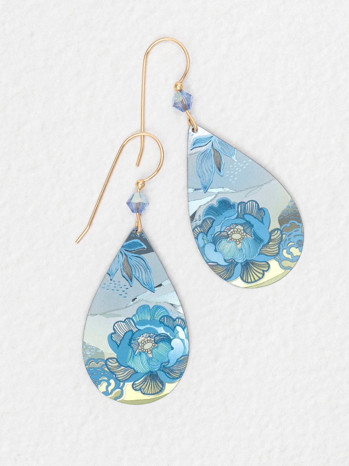 The Cynthia Sky Blue Earrings by Holly Yashi feature gold hooks, blue bead accents, and a sky blue floral pattern with silver on a white textured background. Hypoallergenic and ideal for sensitive ears.