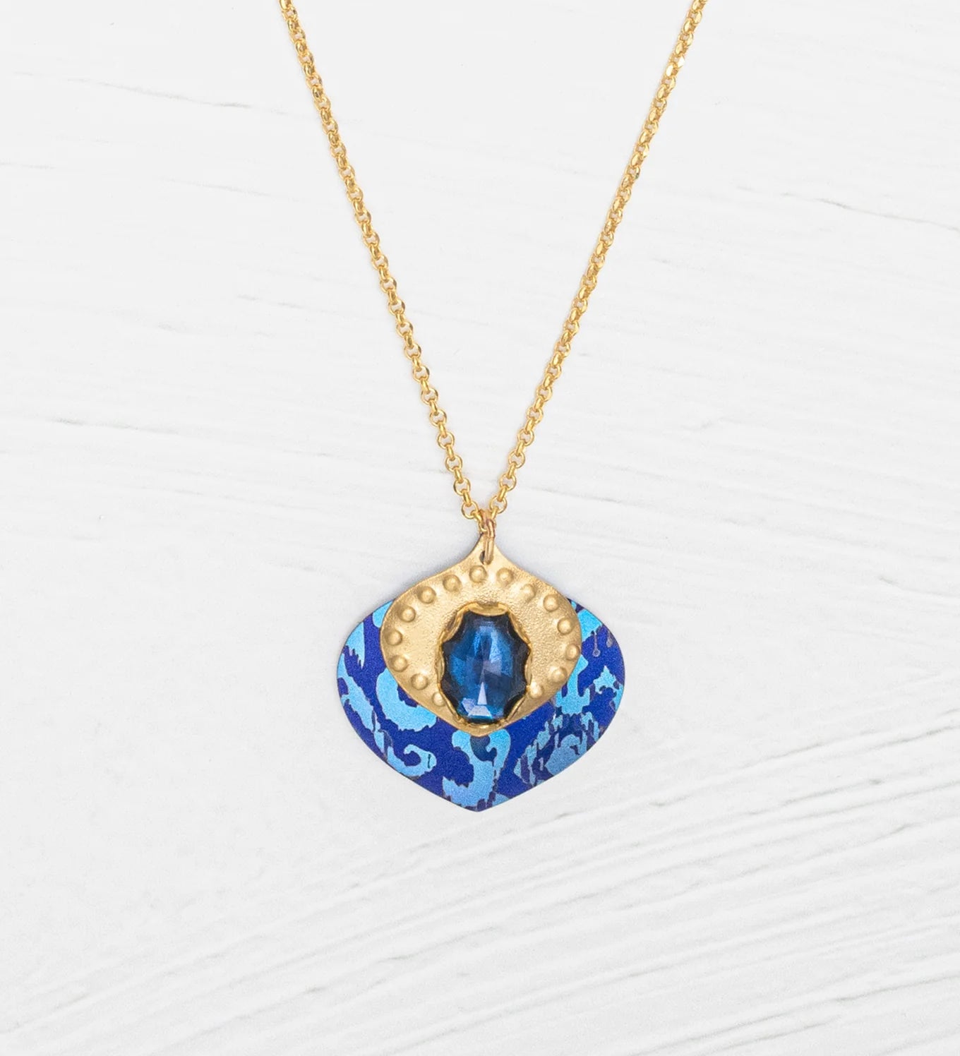 The Arabella Sapphire Blue Necklace by Holly Yashi features a vibrant glass stone set in textured gold with an adjustable pendant for the perfect fit.