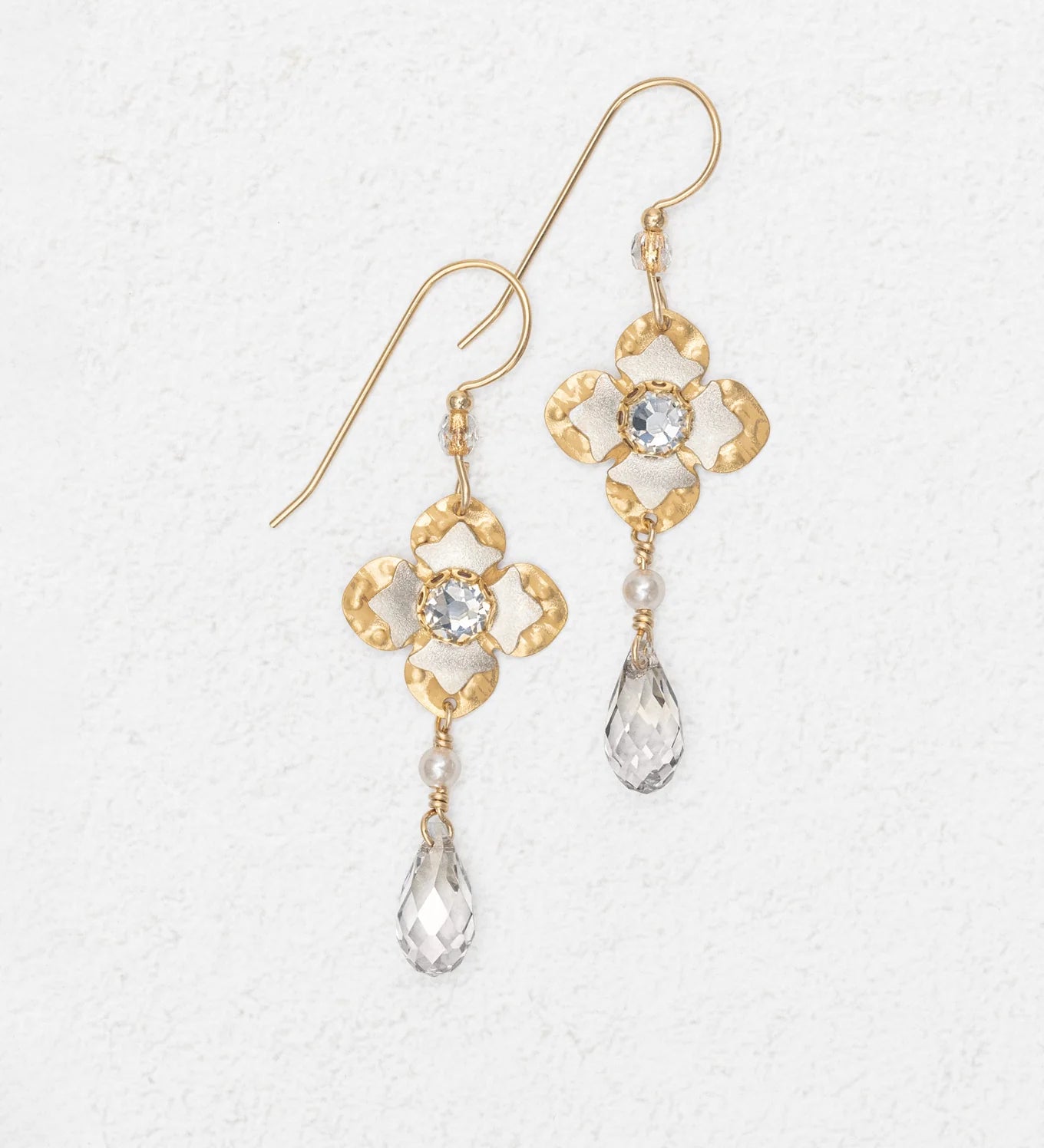 Octavia Gold Silver Earrings by Holly Yashi feature a floral design with a clear central gemstone and teardrop crystal drop, shown on a white textured background.
