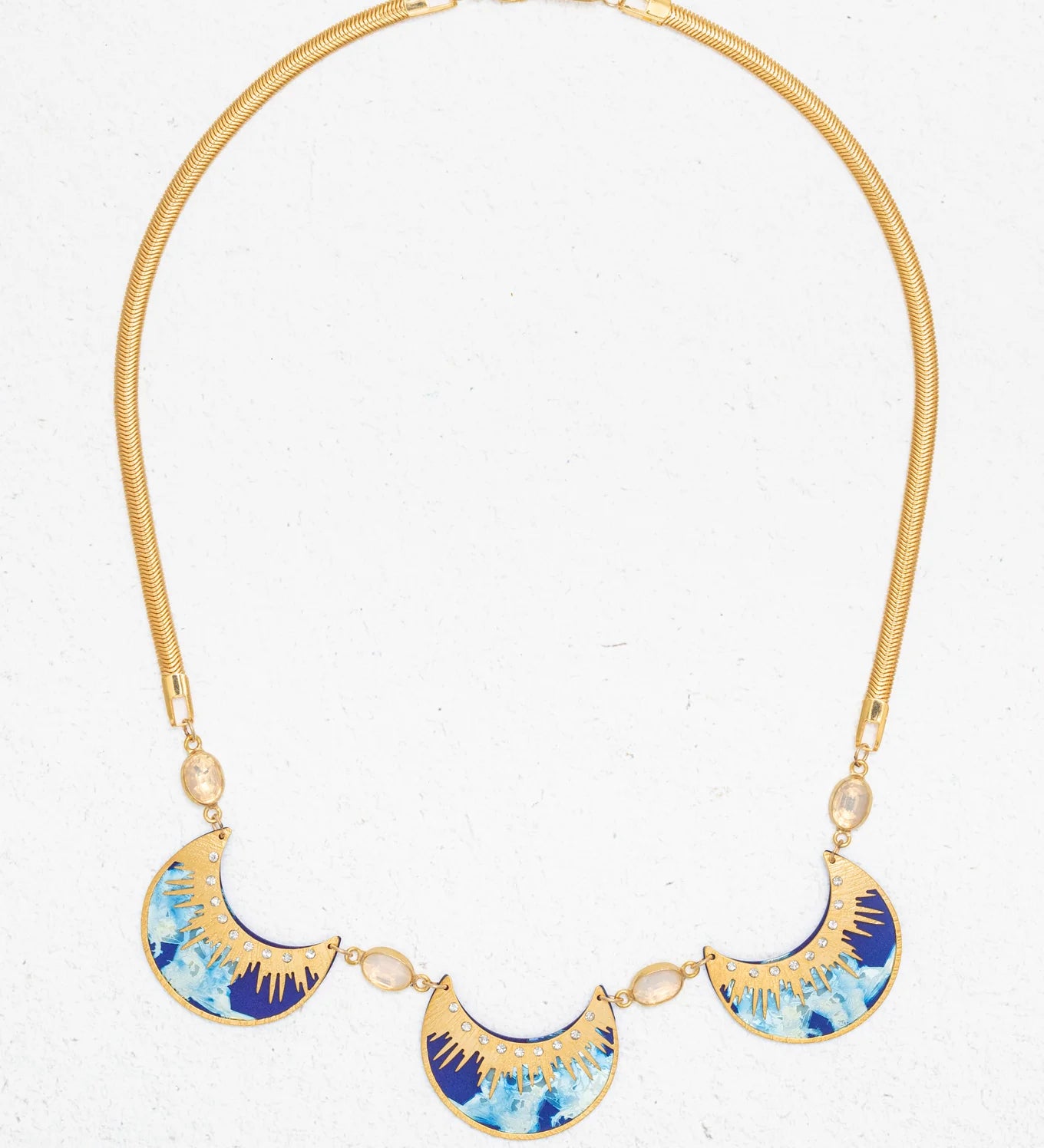 The Selena Necklace-Midnight Blue by Holly Yashi features three crescent blue, turquoise, and gold enamel pendants on a gold snake chain with oval crystal accents, shown on a white background.