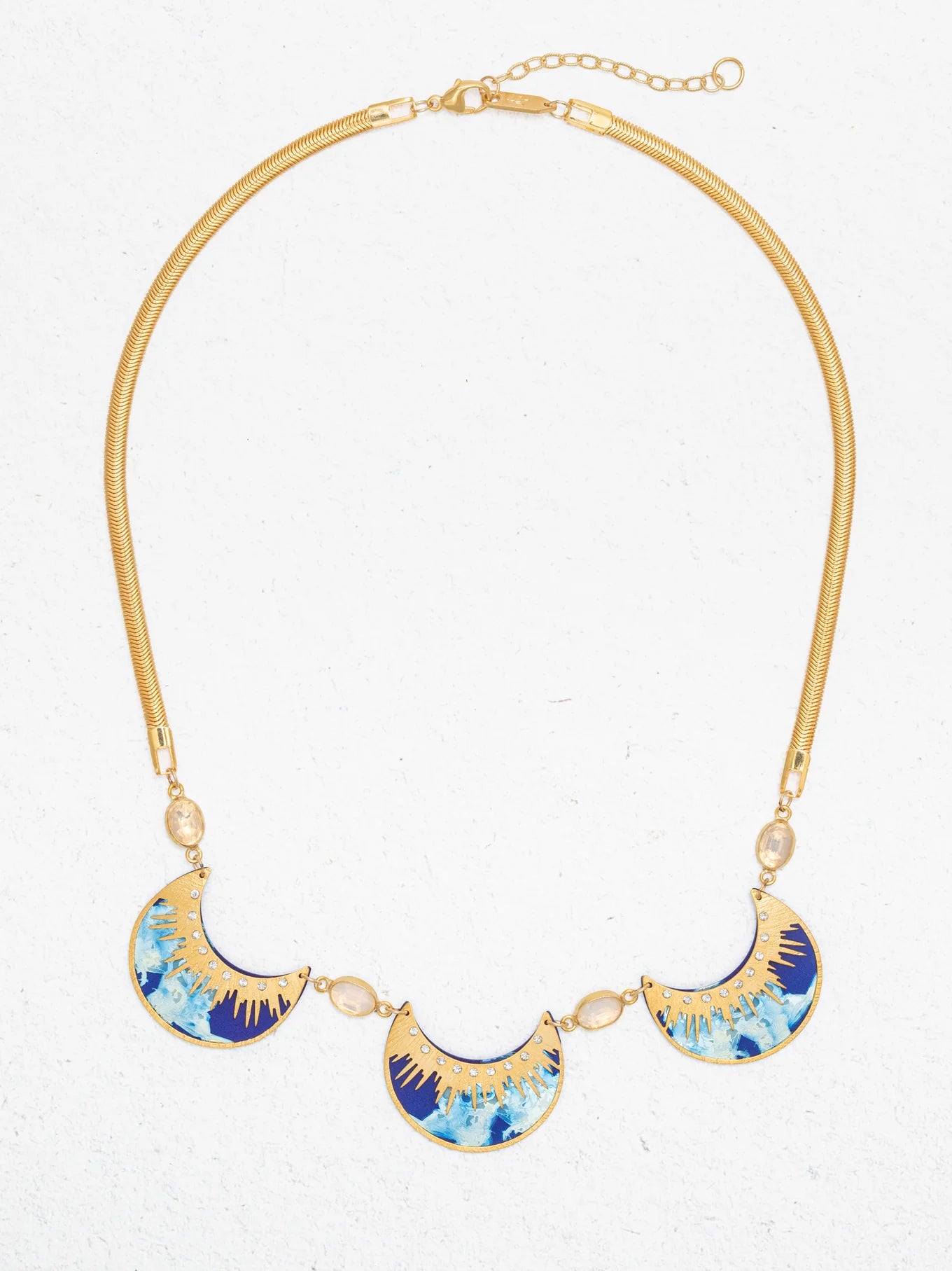 The Selena Necklace-Midnight Blue by Holly Yashi features three crescent blue, turquoise, and gold enamel pendants on a gold snake chain with oval crystal accents, shown on a white background.