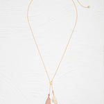The Holly Yashi Special Edition Flutterby Pink Lariat Necklace features a fine gold chain with two pendants—a metallic leaf and a pink-tipped, translucent leaf—displayed on a white textured background.