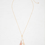 The Holly Yashi Special Edition Flutterby Pink Lariat Necklace features a fine gold chain with two pendants—a metallic leaf and a pink-tipped, translucent leaf—displayed on a white textured background.