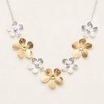 The Plumeria Classic Silver/Gold Necklace by Holly Yashi features alternating gold and silver flower-shaped charms with gemstone centers, beautifully displayed on a light beige background.