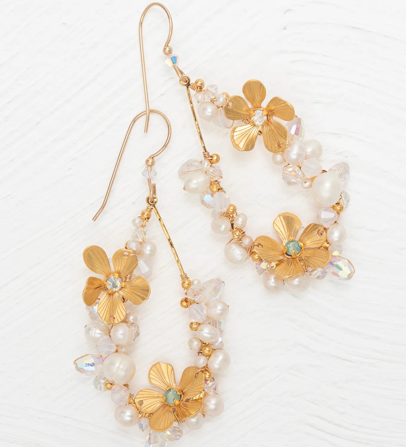 The Rafaela Gold & White Earrings by Holly Yashi feature gold-plated floral designs with delicate petals, small white pearls, and clear beads, shown on a white textured background.