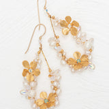 The Rafaela Gold & White Earrings by Holly Yashi feature gold-plated floral designs with delicate petals, small white pearls, and clear beads, shown on a white textured background.
