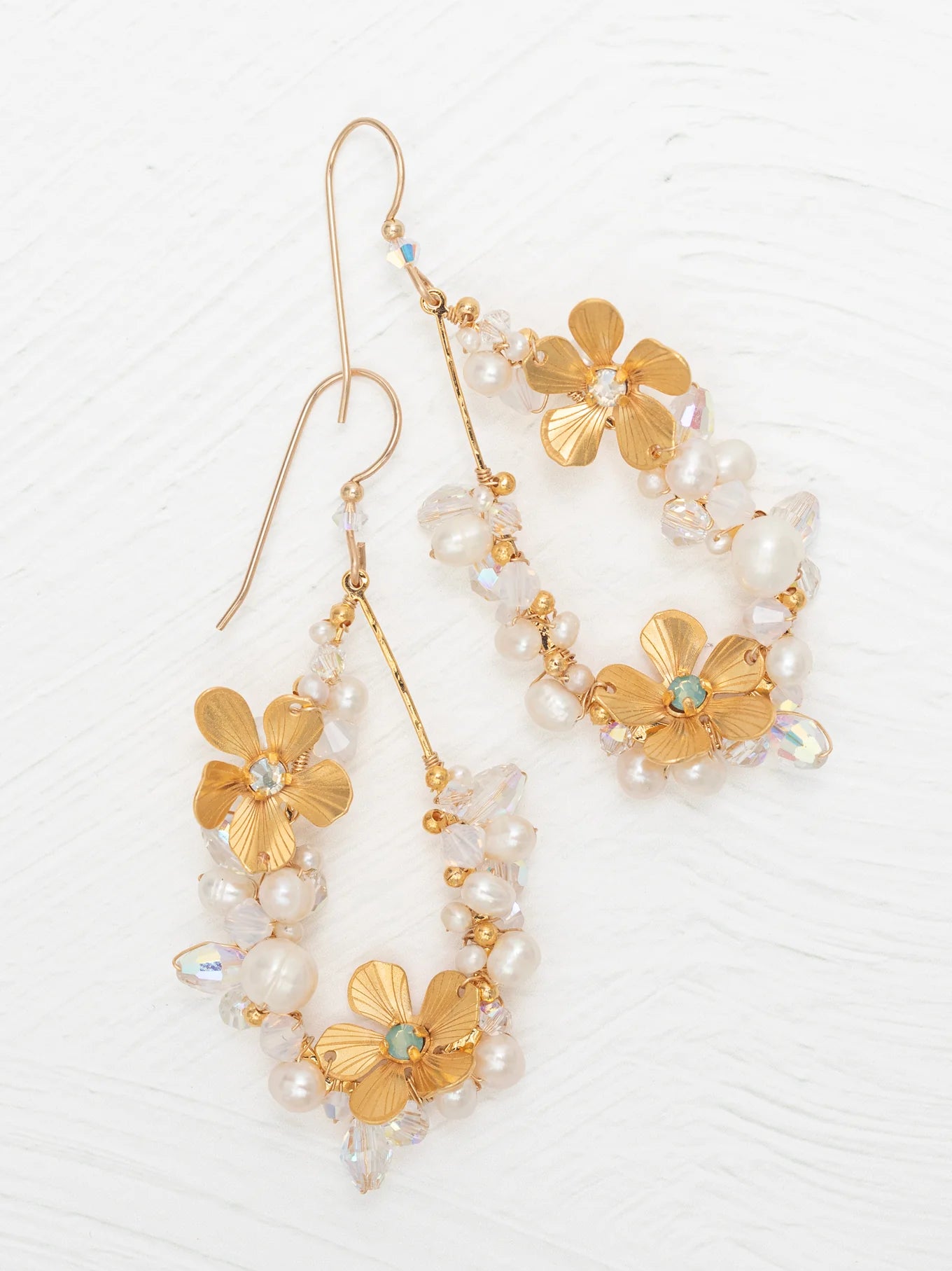 The Rafaela Gold & White Earrings by Holly Yashi feature gold-plated floral designs with delicate petals, small white pearls, and clear beads, shown on a white textured background.