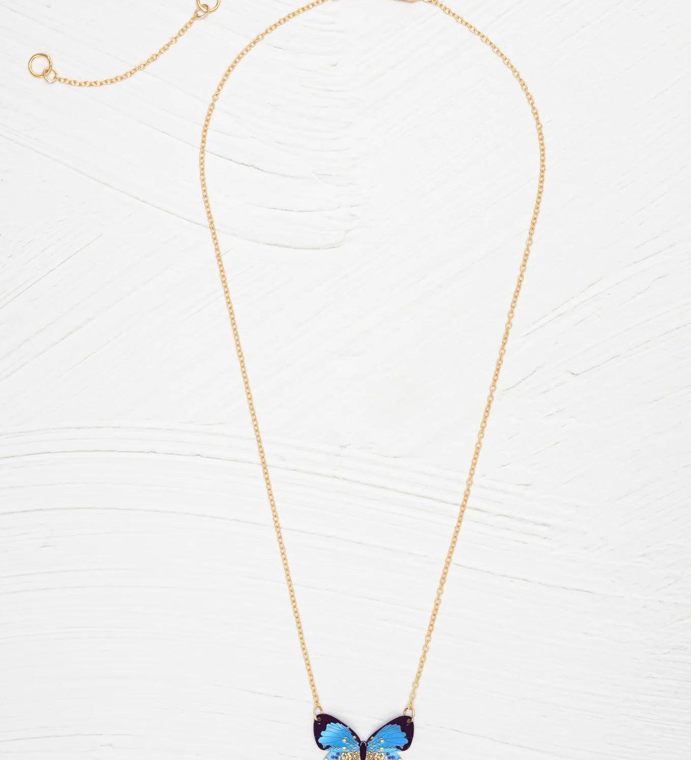 The Blooming Butterfly Blue Radiance Necklace by Holly Yashi features a gold adjustable chain and an iridescent niobium butterfly pendant with gold and turquoise accents, shown on a white textured background—a vibrant statement piece.