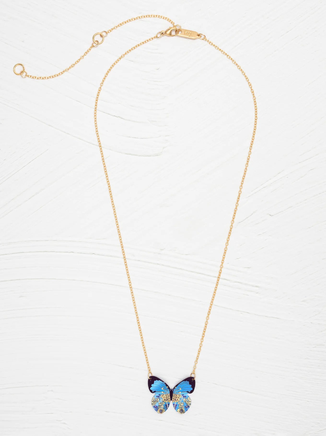 The Blooming Butterfly Blue Radiance Necklace by Holly Yashi features a gold adjustable chain and an iridescent niobium butterfly pendant with gold and turquoise accents, shown on a white textured background—a vibrant statement piece.
