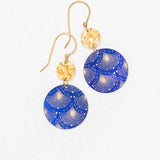 The Danica Earrings in Midnight Blue by Holly Yashi feature handcrafted dangle design with hammered gold circular tops and larger blue round pendants accented by a decorative white and gold fan pattern. Displayed on a white background, these Niobium earrings offer unique style.