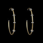 A pair of large, handcrafted Be-Je Designs Gold Filled Matte Hoops with clear rondels is displayed against a black background.