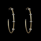 A pair of large, handcrafted Be-Je Designs Gold Filled Matte Hoops with clear rondels is displayed against a black background.