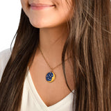 A woman with long brown hair in a white shirt wears the Anne Koplik Designs, Inc. 1/2 Moon Face/Stars Necklace, a gold enameled piece with blue and yellow constellation accents, highlighting elegant handcrafted jewelry.