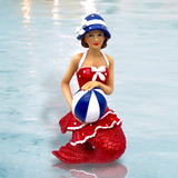 The hand-painted Bathing Beauty Ornament from December Diamonds boasts a red vintage-style swimsuit with white accents, a blue and white striped hat, and a coordinating beach ball, encapsulating holiday decor essence against a water-like backdrop.