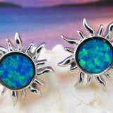 The Jewelry Network Caribbean Opal Sun Post Earrings feature sun-shaped rhodium plated 925 sterling silver with blue-green synthetic opal centers, displayed on a white seashell against a softly blurred gradient background.