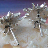 The Caribbean Opal Sun Post Earrings by Jewelry Network, crafted in rhodium plated 925 Sterling Silver with a sunburst design, are displayed on a pale seashell against a softly blurred background in purple, blue, and pink hues.