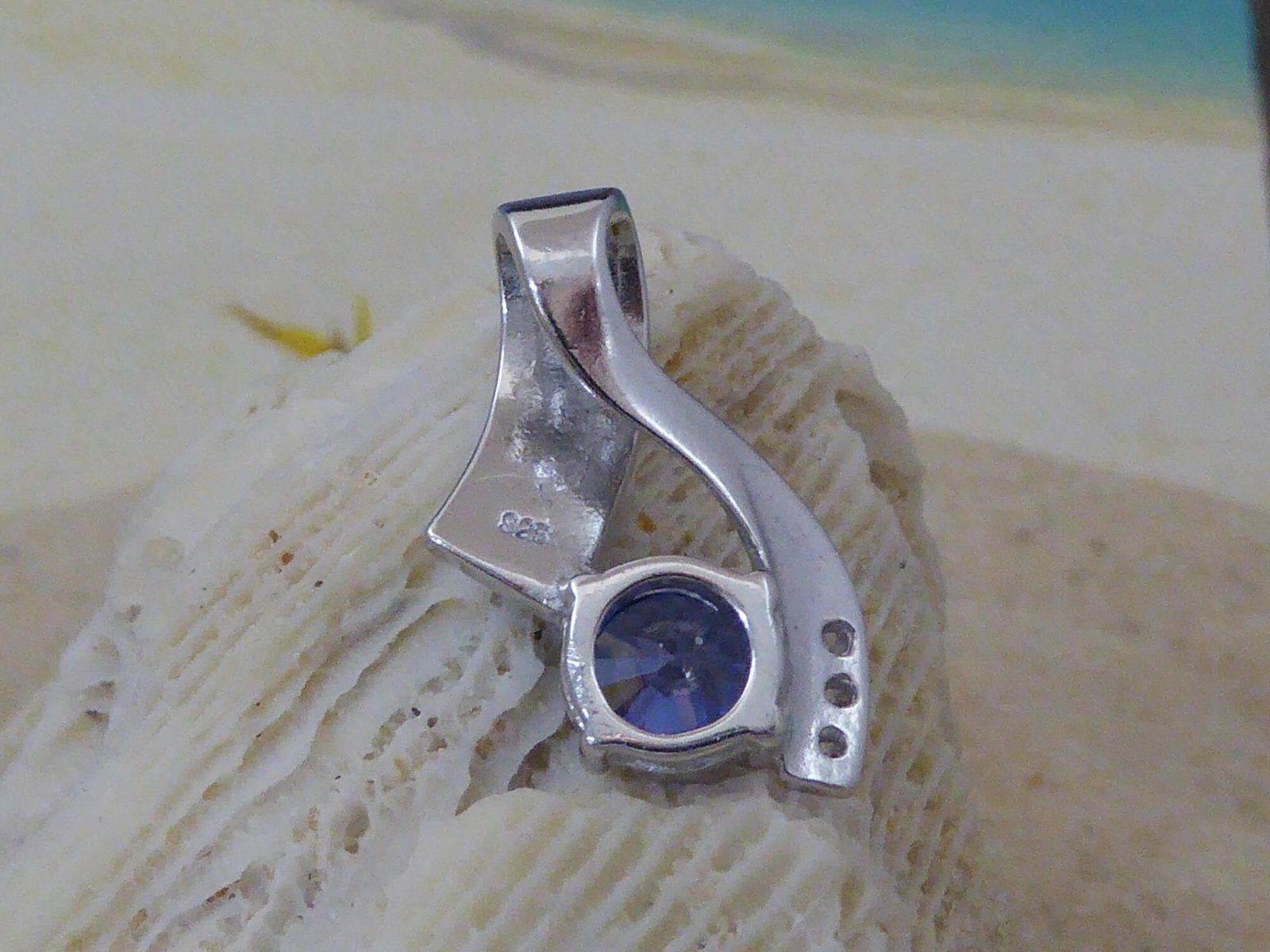 The Jewelry Network Caribbean Opal 3 Triangles/Round Amethyst Pendant rests on a textured white seashell, its modern design highlighted against a softly blurred background of sand with blue and beige accents.