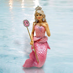 Galinda by December Diamonds is a blonde mermaid doll with a pink crown, dress, and tail, posing gracefully with a jeweled scepter on a shiny blue surface—an ideal addition to any mermaid ornaments collection.