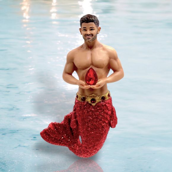 The July Birthstone-Ruby Merman by December Diamonds is a hand-painted figurine with a glittery red tail, holding a ruby ornament, smiling shirtless as he stands in clear blue water.