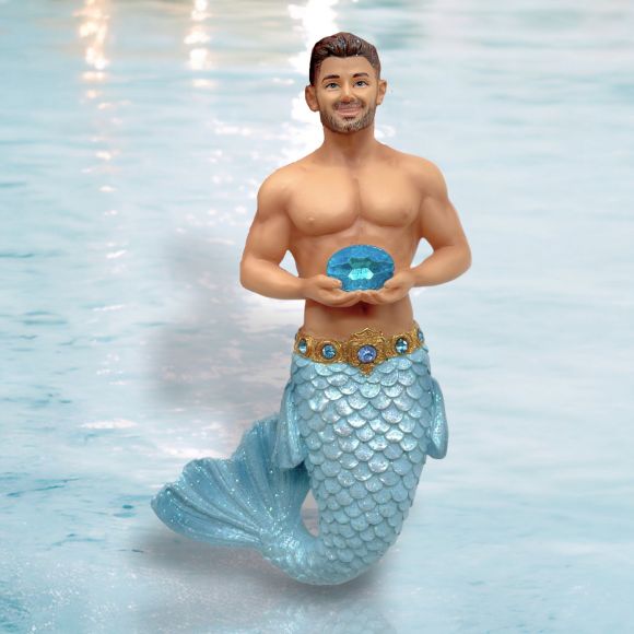 The March Birthstone - Aquamarine Merman by December Diamonds features a merman with a human upper body, blue-scaled tail, gold belt with blue gems, and trimmed beard, holding a blue gem—ideal as festive décor.