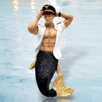 The December Diamonds Mr. Friendly Skies Ornament showcases a muscular merman with a golden-scaled tail, white open shirt, and pilots cap against a blurred water background—perfect for adding magic to your holiday decor.