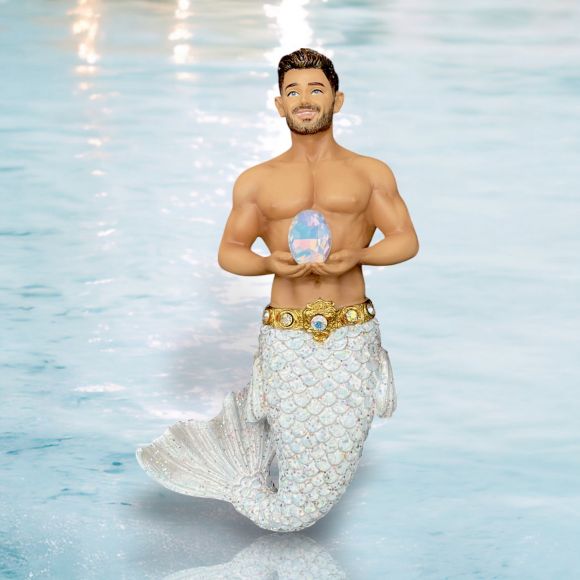 The October Birthstone-Opal Merman by December Diamonds features a light-skinned merman with brown hair and a shiny white tail, standing in blue water and holding a pastel transgender pride egg—an ideal hand-painted ornament.