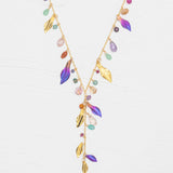 The Holly Yashi Calliope Tropic Punch Necklace showcases a gold-plated chain with gold leaves, colorful beads, and purple enamel niobium leaves in a V-shape on a white background.