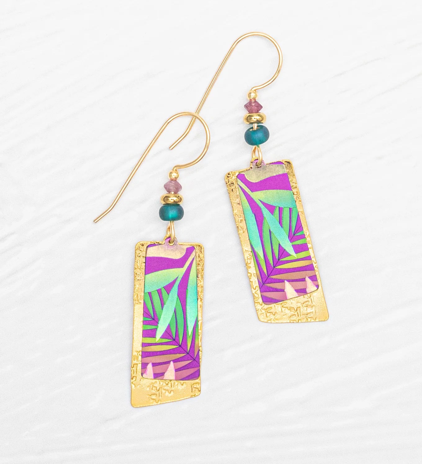 The Davy Rectangles Two Layers - Tropic Magenta Earrings by Holly Yashi feature vibrant purple, green, and teal geometric patterns meticulously crafted as hand-painted earrings. Accented with small teal and gold beads, these rectangular gold earrings are elegantly displayed on a white textured background.