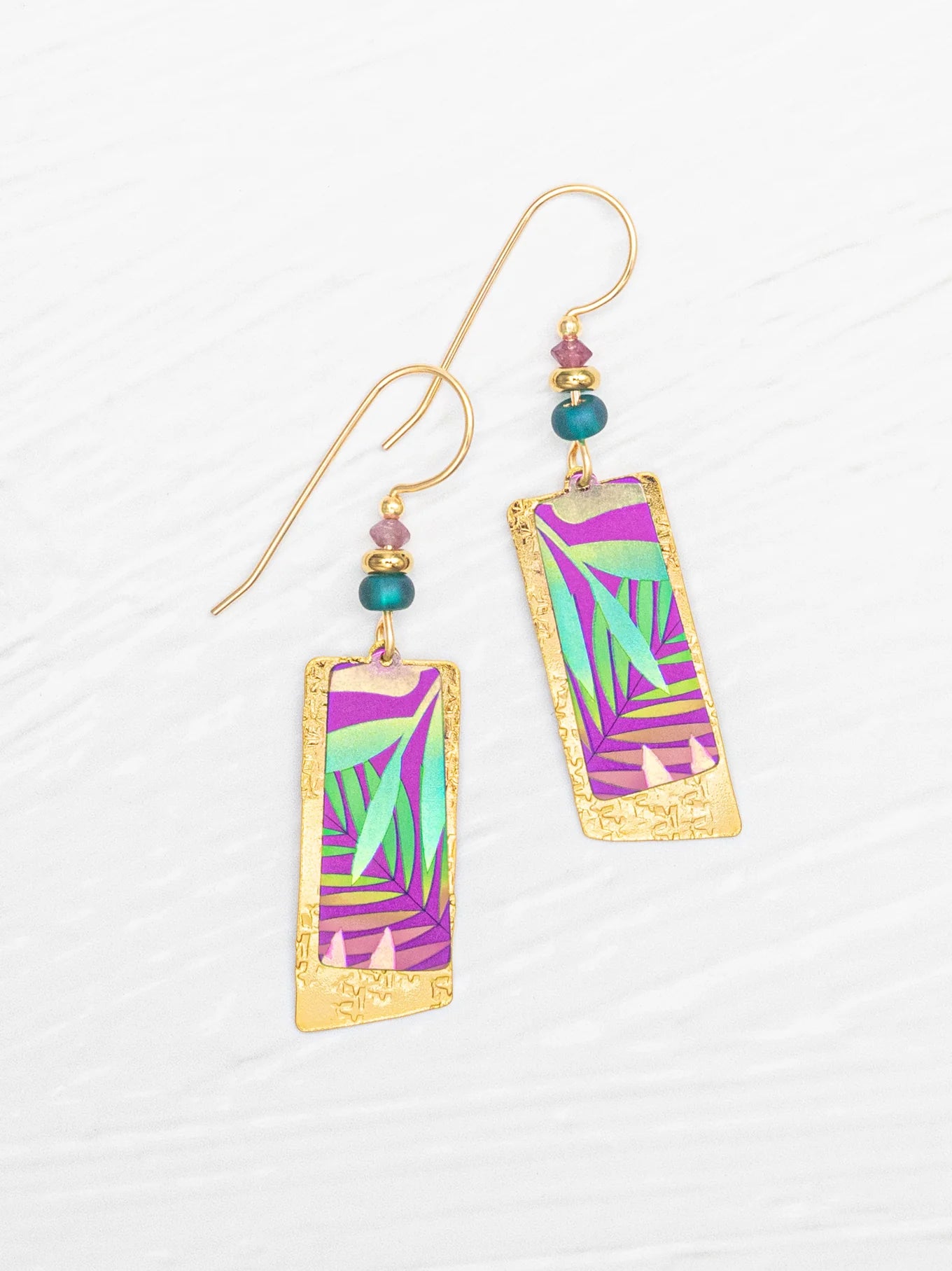 The Davy Rectangles Two Layers - Tropic Magenta Earrings by Holly Yashi feature vibrant purple, green, and teal geometric patterns meticulously crafted as hand-painted earrings. Accented with small teal and gold beads, these rectangular gold earrings are elegantly displayed on a white textured background.