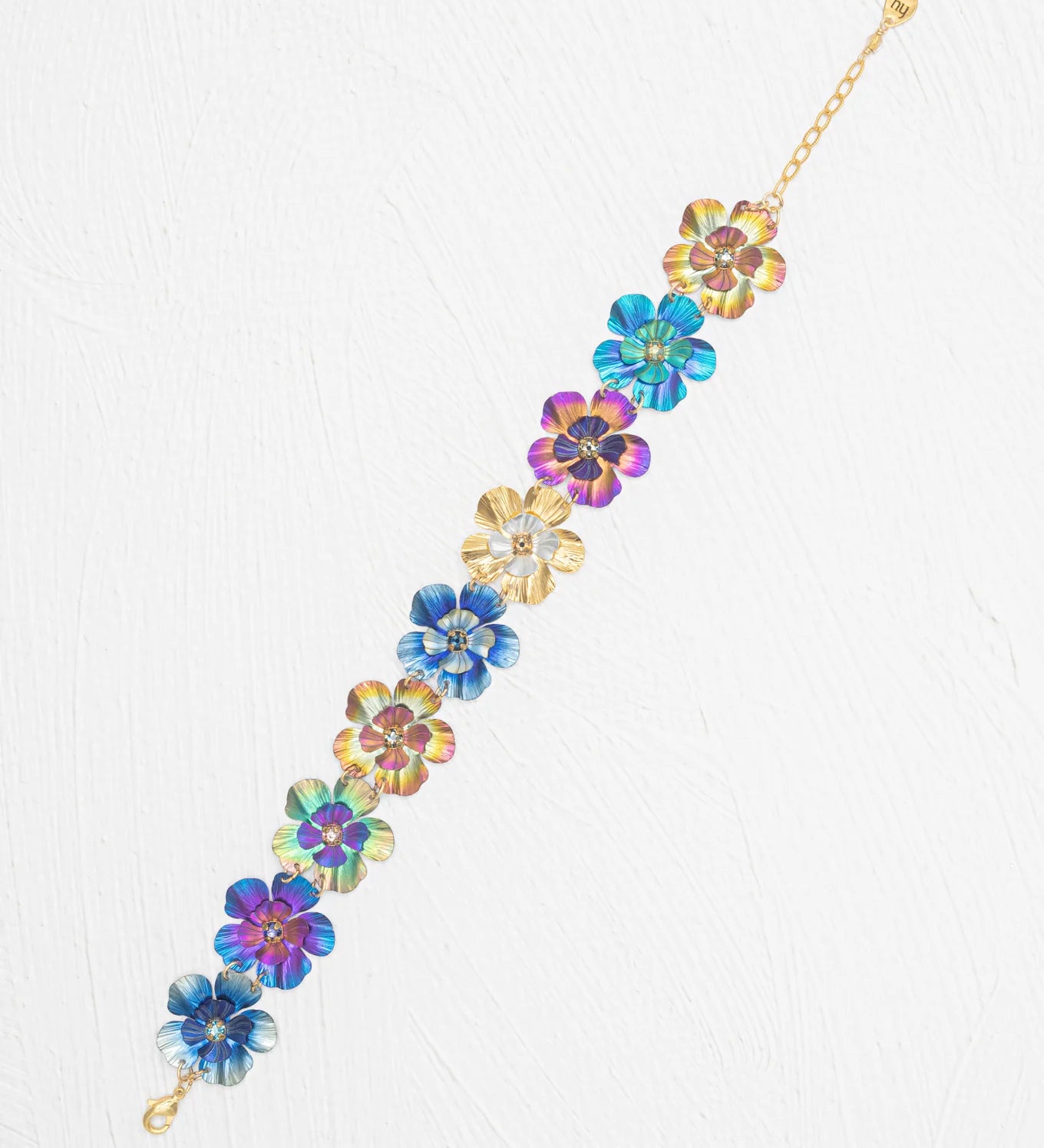The Blissful Bouquet Multicolor Bracelet by Holly Yashi is a gold chain adorned with iridescent niobium flowers, displayed on a white textured background. Handcrafted, this vibrant piece brings colorful charm to any outfit.