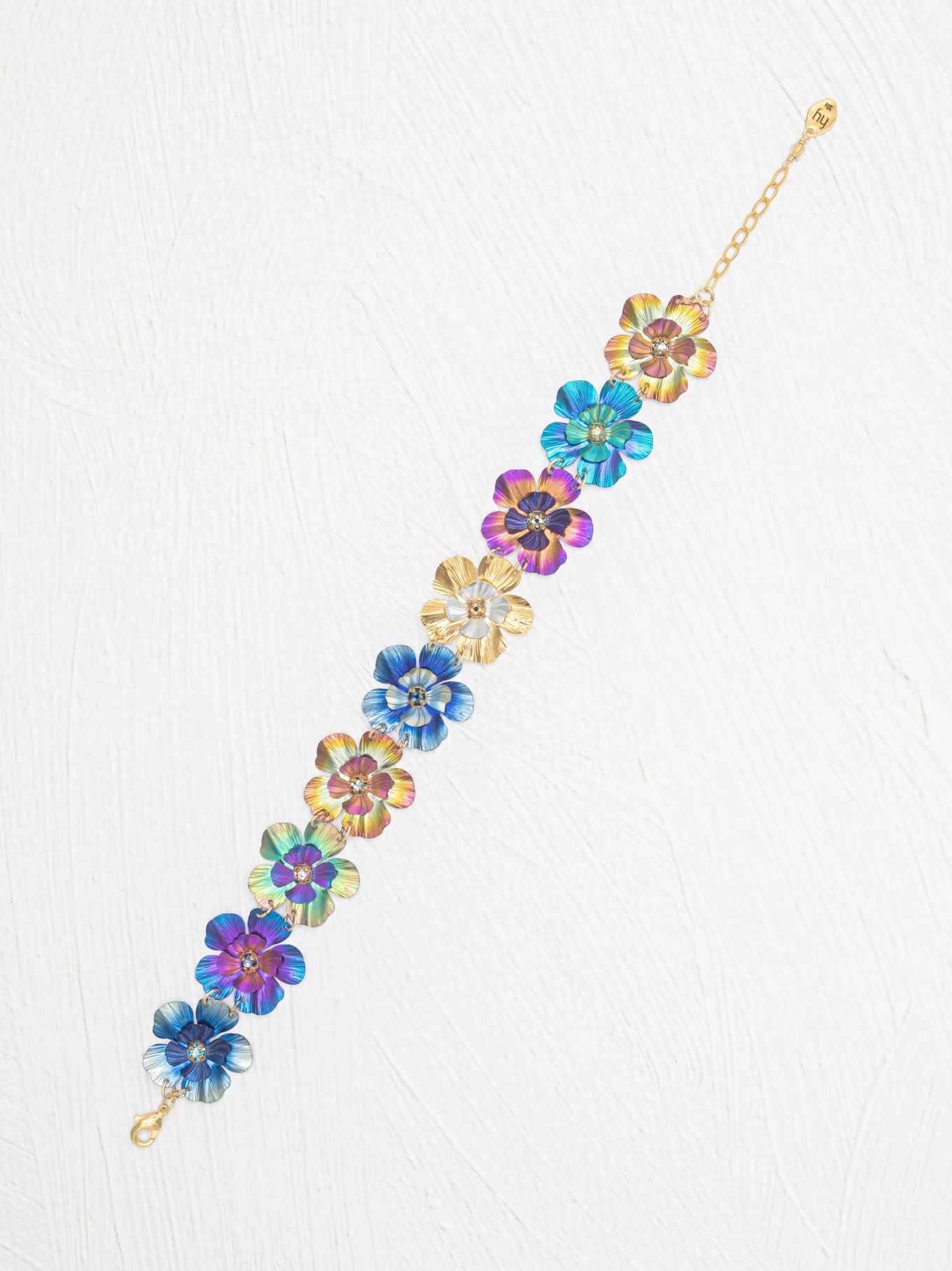 The Blissful Bouquet Multicolor Bracelet by Holly Yashi is a gold chain adorned with iridescent niobium flowers, displayed on a white textured background. Handcrafted, this vibrant piece brings colorful charm to any outfit.