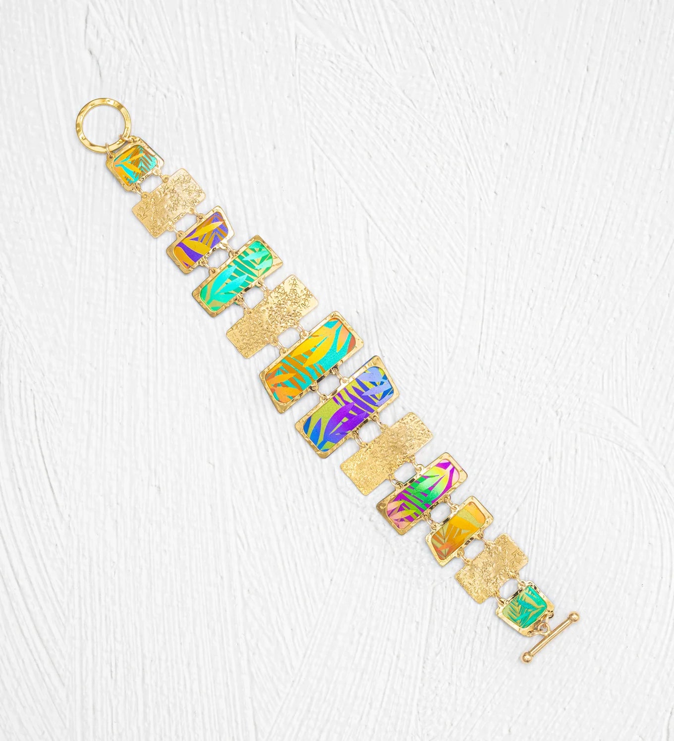 The Mahana Bracelet - 12 Rectangular Panels by Holly Yashi features rectangular, multicolored enamel panels and textured gold links, creating a vibrant tropical accessory beautifully displayed on a white textured background.