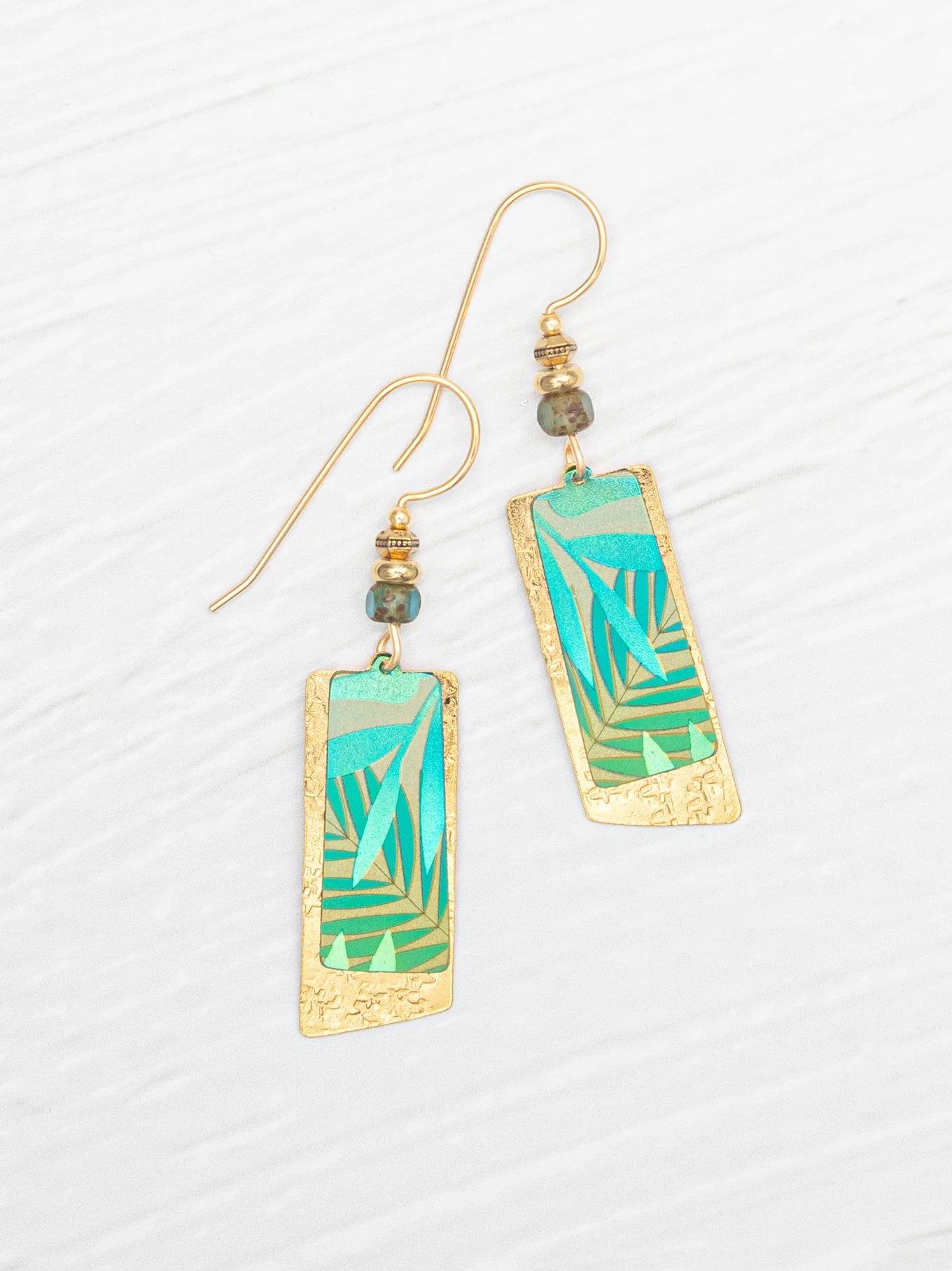Introducing the Holly Yashi Davy Rectangles Two Layers - Tropic Green Earrings: hand-painted gold earrings featuring layered rectangular shapes with abstract green and teal geometric designs. Each earring is accented with a delicate beaded detail above the rectangles and finished with gold hooks, beautifully displayed on a white textured background. These striking accessories are perfect for any occasion.