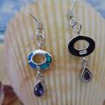 Jewelry Network’s Caribbean Opal Oval w/Amethyst Teardrop Dangle Earrings are shown before a seashell, with the beach and ocean softly blurred in the background.