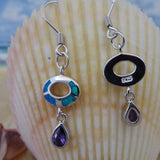 Jewelry Network’s Caribbean Opal Oval w/Amethyst Teardrop Dangle Earrings are shown before a seashell, with the beach and ocean softly blurred in the background.