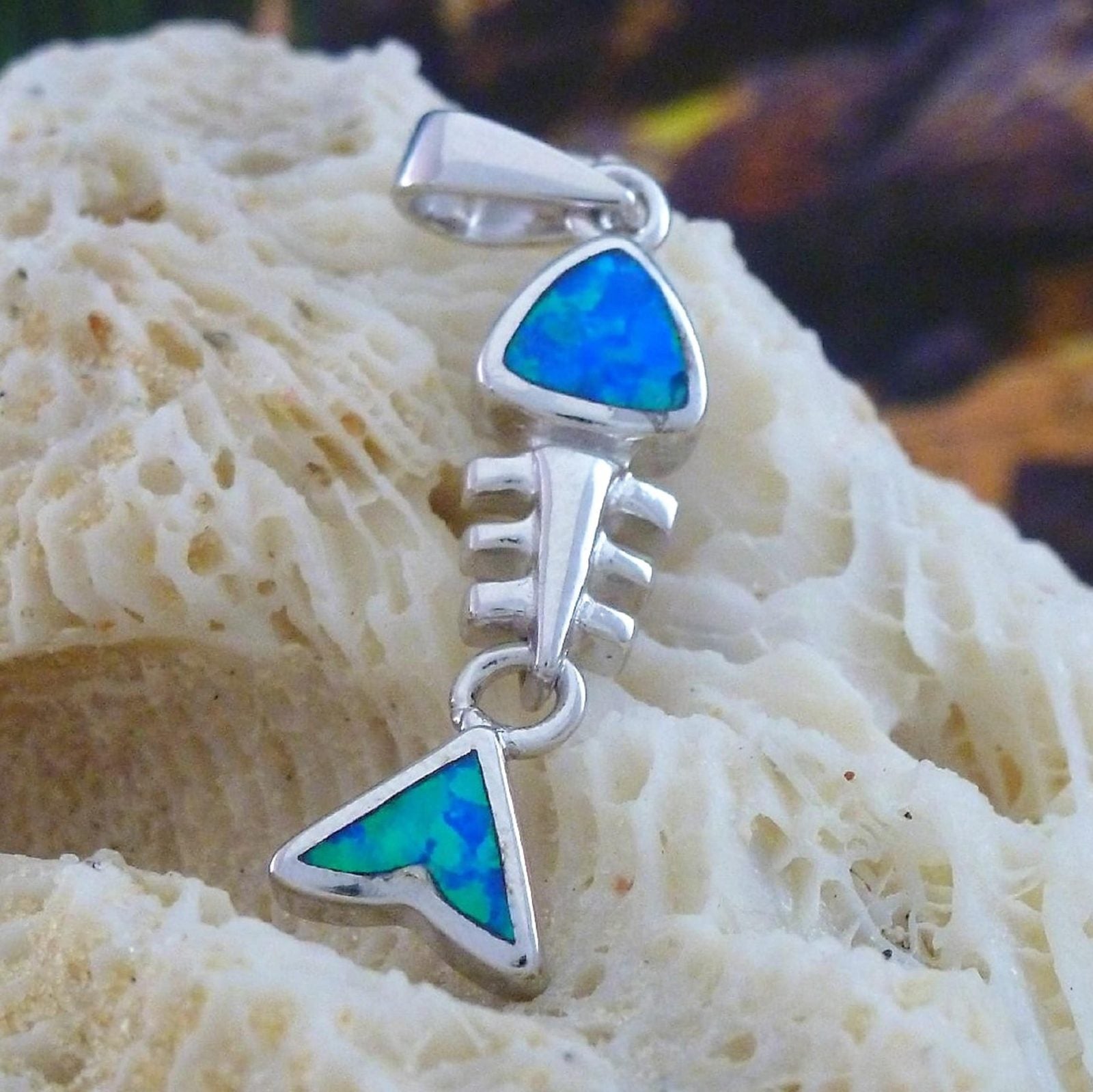 The Jewelry Network's Caribbean Opal Fish Bones-Pendant ONLY features a sterling silver fishbone design with geometric shapes, intricate details, and shimmering blue-green opal inlays, displayed on a textured cream surface.