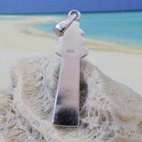 The Caribbean Opal Lighthouse-Pendant ONLY by Jewelry Network, crafted in sterling silver and marked 925, rests on textured white coral with a sandy beach and blue ocean blurred in the background—a striking nautical accessory.