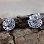 Close-up of Jewelry Network’s Caribbean Opal Round w/CZ Surround Post Earrings' 925 sterling silver backs on textured wood, highlighting the perforated circular design with a softly blurred background.